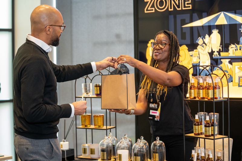 Man and woman interacting with a brown paper bag in a store setting with product displays
