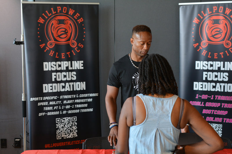 Two people interacting at a Willpower Athletics event with promotional banners in the background.