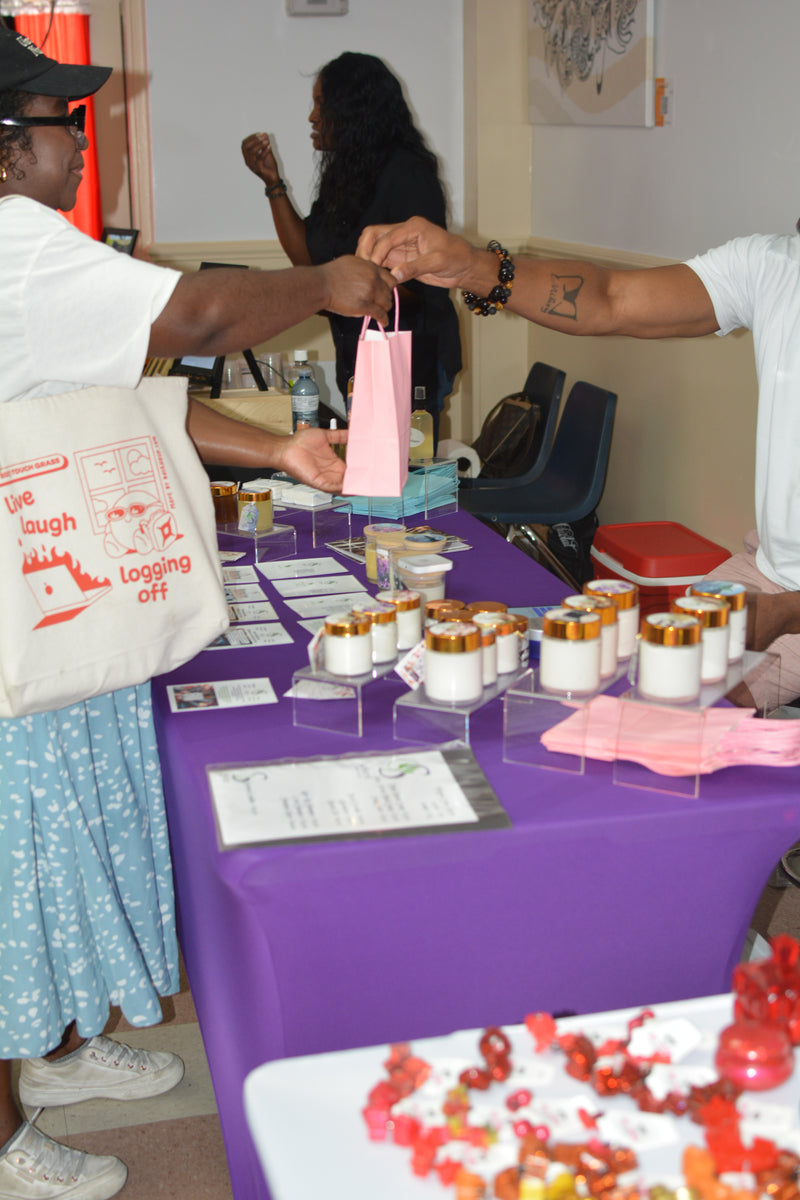 Two people interacting over a table with small containers and a pink bag.