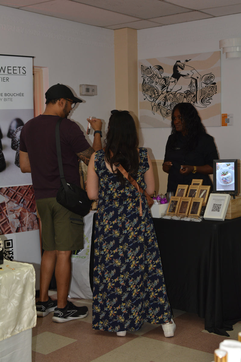 People interacting at an event with a table displaying items and a poster on the wall.