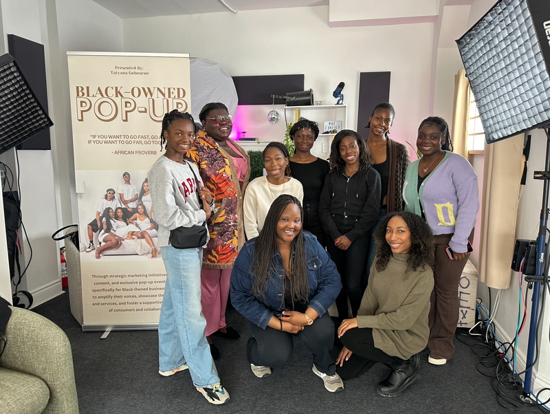 Group of women posing in a studio setting with promotional materials and equipment.