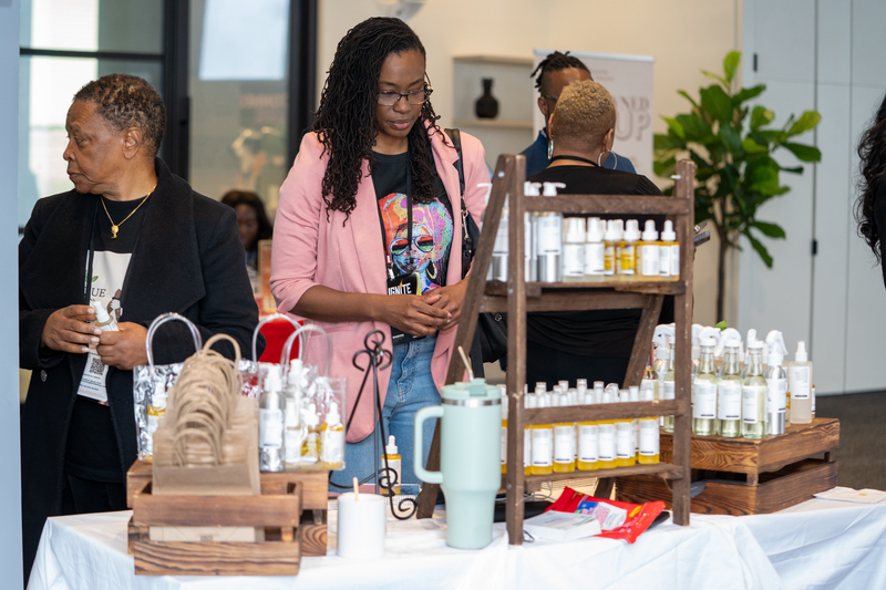Woman examining products at a trade show booth with various items on display.
