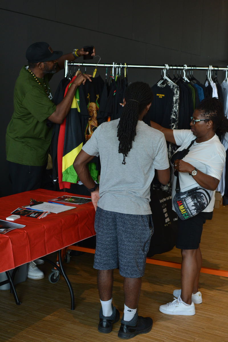 People browsing through clothing at a market stall with a table displaying items.